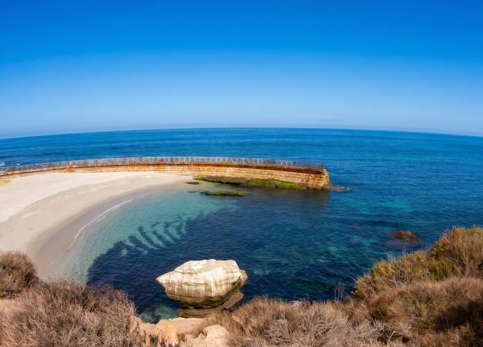 La Jolla Cove in San Diego — the seawall curving around turquoise water with a white boulder in the shallows.