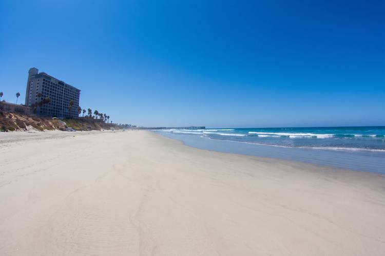 Law St surf break in Pacific Beach, San Diego — waves breaking onto wet sand with Crystal Pier in the distance.